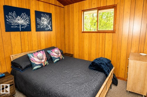Wood-paneled bedroom featuring a sloped wood-finish ceiling, a window with wood trim, and textured carpeting - 27 Point Drive, Rural St. Paul County, AB - Indoor
