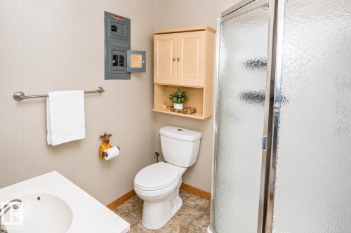 Bathroom featuring a white toilet, enclosed shower with textured glass, light wood-finish wall cabinet, and a vanity with an integrated white sink - 27 Point Drive, Rural St. Paul County, AB - Indoor Photo Showing Bathroom