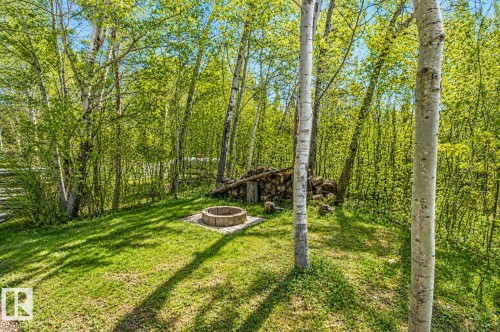 Private outdoor space featuring a stone fire pit, surrounded by lush green foliage and mature trees - 27 Point Drive, Rural St. Paul County, AB - Outdoor