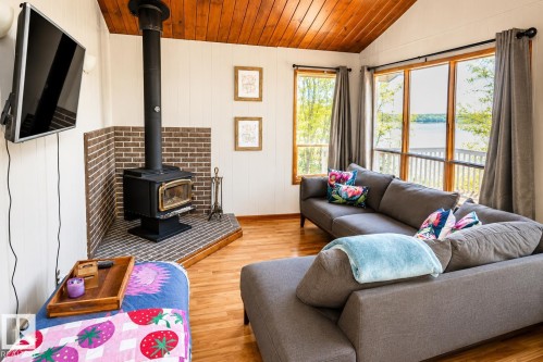 Living area featuring a wood-burning stove with a brick surround, hardwood flooring, and a vaulted wood-paneled ceiling - 27 Point Drive, Rural St. Paul County, AB - Indoor Photo Showing Living Room With Fireplace