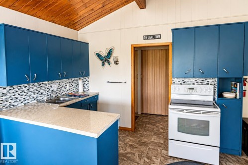 Kitchen featuring bright blue cabinetry, a neutral-toned countertop, and a mosaic tile backsplash - 27 Point Drive, Rural St. Paul County, AB - Indoor Photo Showing Kitchen With Double Sink