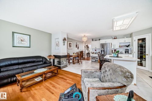 Open-concept living space featuring wood-finish flooring, a built-in fireplace with a stone hearth, and light gray wall tones - 168 Kulawy Drive N, Edmonton, AB 