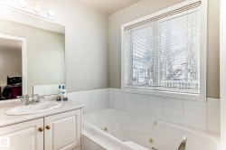 Bathroom featuring a white jetted tub, a single window with blinds, and a vanity with an integrated sink and base cabinetry - 