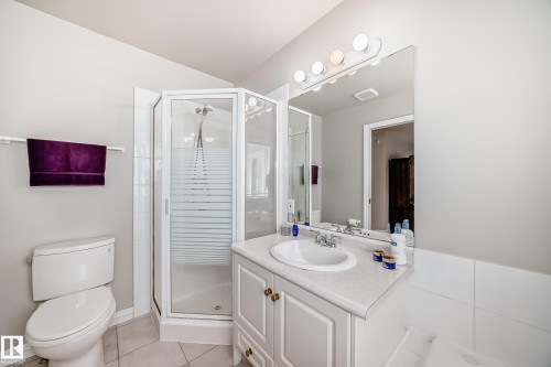 Bathroom featuring a glass-enclosed corner shower, single vanity with a white countertop and integrated sink, vanity lighting, a large mirror, and tiled flooring - 168 Kulawy Drive N, Edmonton, AB 
