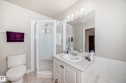 Bathroom featuring a glass-enclosed corner shower, single vanity with a white countertop and integrated sink, vanity lighting, a large mirror, and tiled flooring - 