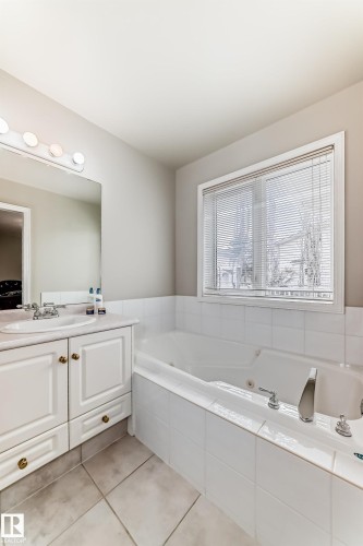 Soaking tub with white tile surround, single window with blinds, white vanity with integrated sink, and tile flooring - 168 Kulawy Drive N, Edmonton, AB 
