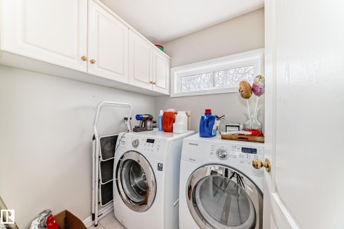 Dedicated laundry space featuring white cabinetry with gold-toned hardware, a window offering natural light, and tile flooring - 168 Kulawy Drive N, Edmonton, AB 