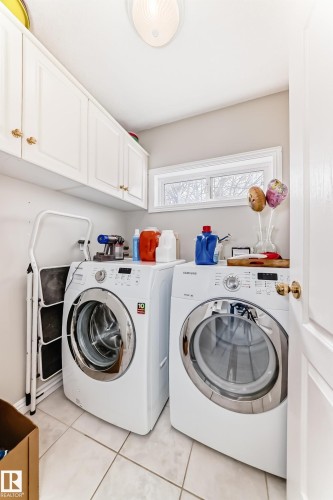Dedicated laundry space featuring white cabinetry with gold-tone hardware, a rectangular window, and tile flooring - 168 Kulawy Drive N, Edmonton, AB 