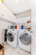 Dedicated laundry space featuring white cabinetry with gold-tone hardware, a rectangular window, and tile flooring - 