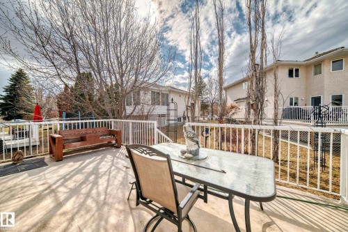 Expansive concrete patio featuring white railing, mature trees, and a beige stucco exterior - 168 Kulawy Drive N, Edmonton, AB 