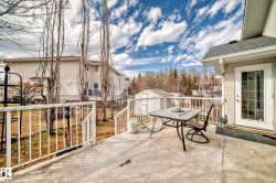 Concrete deck with white railing, featuring an exterior door with glass paneling, a shingled roofline, and a storage shed - 