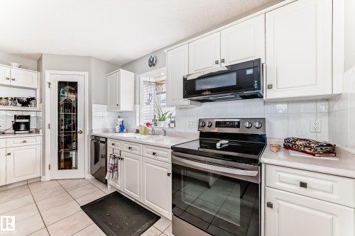 Kitchen featuring white cabinetry, stainless steel range, built-in microwave, light countertops, and a full-light pantry door - 168 Kulawy Drive N, Edmonton, AB 
