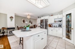 Kitchen featuring a central island with countertop seating, white cabinetry, stainless steel appliances, and a tiled floor - 