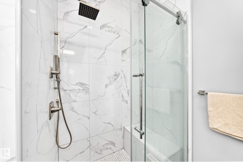 Shower enclosure featuring large format white marble-patterned tile, a rain showerhead, and a handheld shower fixture - 1781 Melrose Crescent, Edmonton, AB 
