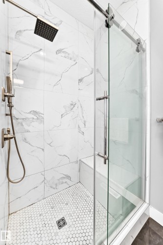 Shower enclosure featuring white marble-look tile walls, a built-in shower bench, and a hexagonal mosaic tile floor - 1781 Melrose Crescent, Edmonton, AB 