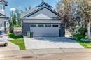 Contemporary residential exterior featuring a light gray garage door with upper window inserts, dark stone veneer accents, light gray horizontal siding, and a dark shingled roof with a prominent gable - 1781 Melrose Crescent, Edmonton, AB 