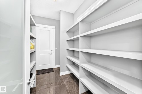 Pantry featuring extensive built-in shelving, durable tile flooring, white shaker-style door, white door trim, and recessed lighting - 1781 Melrose Crescent, Edmonton, AB 