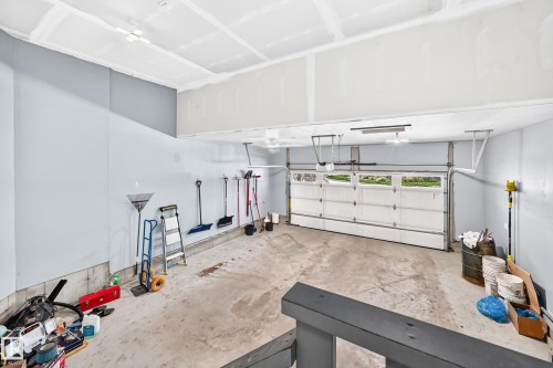 Spacious garage with exposed beam ceiling, light-toned walls, concrete flooring, and a white paneled garage door with upper window inserts - 1781 Melrose Crescent, Edmonton, AB 
