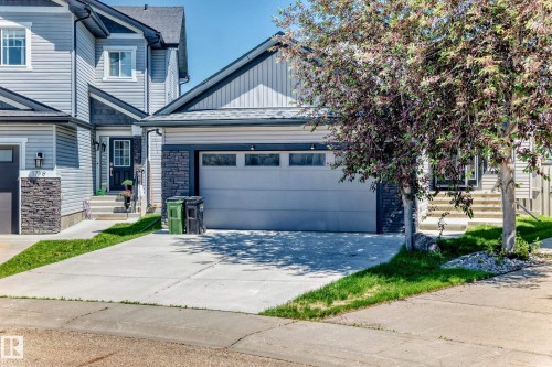 Contemporary exterior featuring light gray siding with dark gray stone accents, a double-width driveway, a two-car garage with horizontal paneling, and a covered entry with a paneled door - 1781 Melrose Crescent, Edmonton, AB 