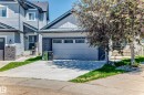 Contemporary exterior featuring light gray siding with dark gray stone accents, a double-width driveway, a two-car garage with horizontal paneling, and a covered entry with a paneled door - 1781 Melrose Crescent, Edmonton, AB 