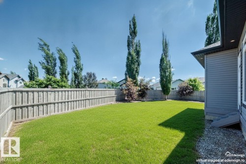 Expansive backyard featuring a lush lawn, vertical wood fencing, mature trees, and a gravel perimeter alongside the home's siding - 1781 Melrose Crescent, Edmonton, AB 