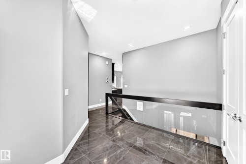 Hallway featuring dark large-format tile flooring, light grey walls, and a modern glass and black metal railing - 1781 Melrose Crescent, Edmonton, AB 