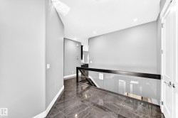 Hallway featuring dark large-format tile flooring, light grey walls, and a modern glass and black metal railing - 