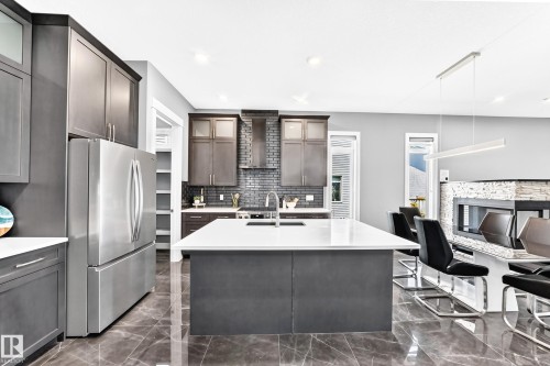 Expansive kitchen featuring a large central island with seating, stainless steel appliances, dark grey cabinetry, and sleek tile flooring - 1781 Melrose Crescent, Edmonton, AB 