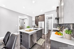 Contemporary kitchen featuring an expansive center island with an undermount sink, stainless steel appliances, dark wood-finish cabinetry, white countertops, and a subway tile backsplash - 