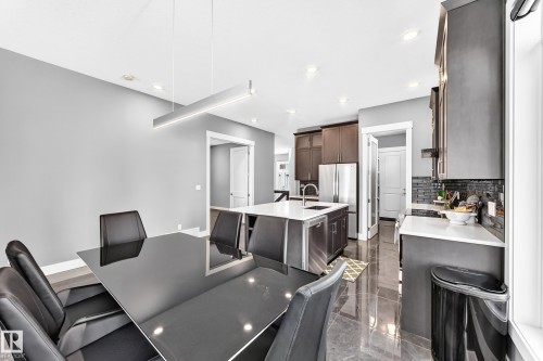 Spacious dining area featuring a modern linear pendant light and a sleek black table - 1781 Melrose Crescent, Edmonton, AB 