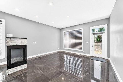 Spacious room featuring polished stone-finish flooring, a contemporary fireplace with stacked stone surround, recessed ceiling lighting, and a glass-paneled exterior door - 1781 Melrose Crescent, Edmonton, AB 