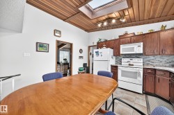 Kitchen featuring a wood-panel ceiling, skylight, white appliances, dark wood-finish cabinetry, and a mosaic tile backsplash - 