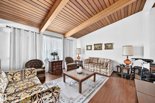 Living space featuring a vaulted wood-slat ceiling with exposed beams, wood-finish flooring, white walls, and vertical blinds on a large window - 13804 87 Street, Edmonton, AB 