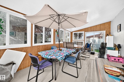 Sunroom featuring wood-finish wall paneling, multiple windows, and a sliding glass door - 13804 87 Street, Edmonton, AB 