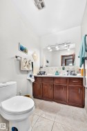 Bathroom featuring a dual-sink vanity with wood cabinetry, a large mirror, track lighting, and tiled flooring - 