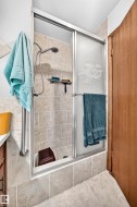 Tiled shower enclosure featuring a sliding glass door with frosted accent, a handheld showerhead, and a built-in shower caddy - 