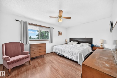 Spacious bedroom featuring wood-finish flooring, a large window with natural light, a ceiling fan with integrated lighting, and neutral wall finishes - 13804 87 Street, Edmonton, AB 