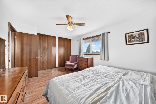Bedroom featuring warm wood-finish flooring, a ceiling fan with integrated lighting, and multiple bi-fold closet doors - 13804 87 Street, Edmonton, AB 