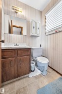 Bathroom featuring a wood vanity with a light-colored countertop, wall-mounted mirror, and overhead light fixture - 