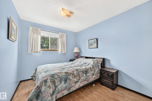 Bedroom featuring wood-finish flooring, light blue painted walls, a window with a white curtain, and a ceiling-mounted light fixture - 13804 87 Street, Edmonton, AB 