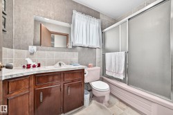 Bathroom featuring a wood-finish vanity with a laminate countertop, an integrated sink, a full-width mirror, and a shower-tub combination with frosted sliding doors - 