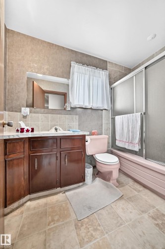 Bathroom featuring a wood-finish vanity with a built-in sink, a tiled countertop, and a mirrored wall - 13804 87 Street, Edmonton, AB 