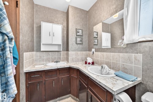 Bathroom featuring two oval undermount sinks, a corner vanity with wood-finish cabinetry, and a large wall-mounted mirror - 13804 87 Street, Edmonton, AB 