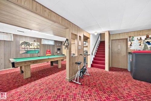Recreation space featuring wood-finish wall paneling, a red patterned carpet, and a built-in shelf bar area - 13804 87 Street, Edmonton, AB 