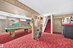 Recreation space featuring wood-finish wall paneling, a red patterned carpet, and a built-in shelf bar area - 