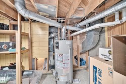 Utility room featuring a water heater, exposed ductwork, and overhead piping - 