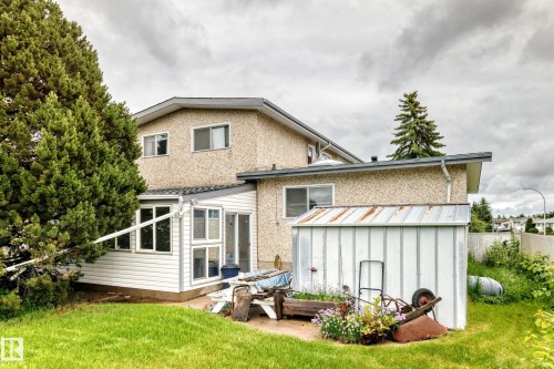 Rear exterior featuring a sunroom addition with multiple windows, stucco and siding finishes, and a detached metal shed - 13804 87 Street, Edmonton, AB 