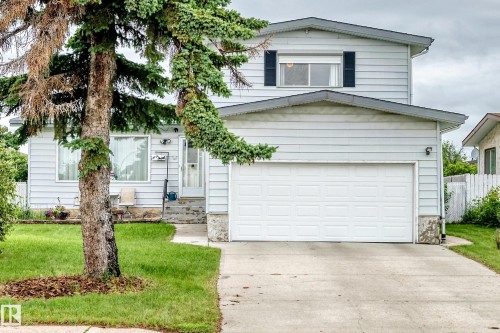 Two-story property featuring light-colored siding, a prominent attached garage with a white door, and a concrete driveway - 13804 87 Street, Edmonton, AB 