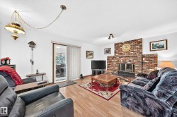 Living area featuring a brick fireplace, light wood-finish flooring, white walls, and a sliding glass door - 