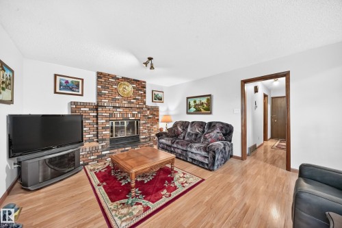 Living area featuring a brick fireplace with a raised hearth, wood-finish flooring, white walls, and dark wood trim - 13804 87 Street, Edmonton, AB 